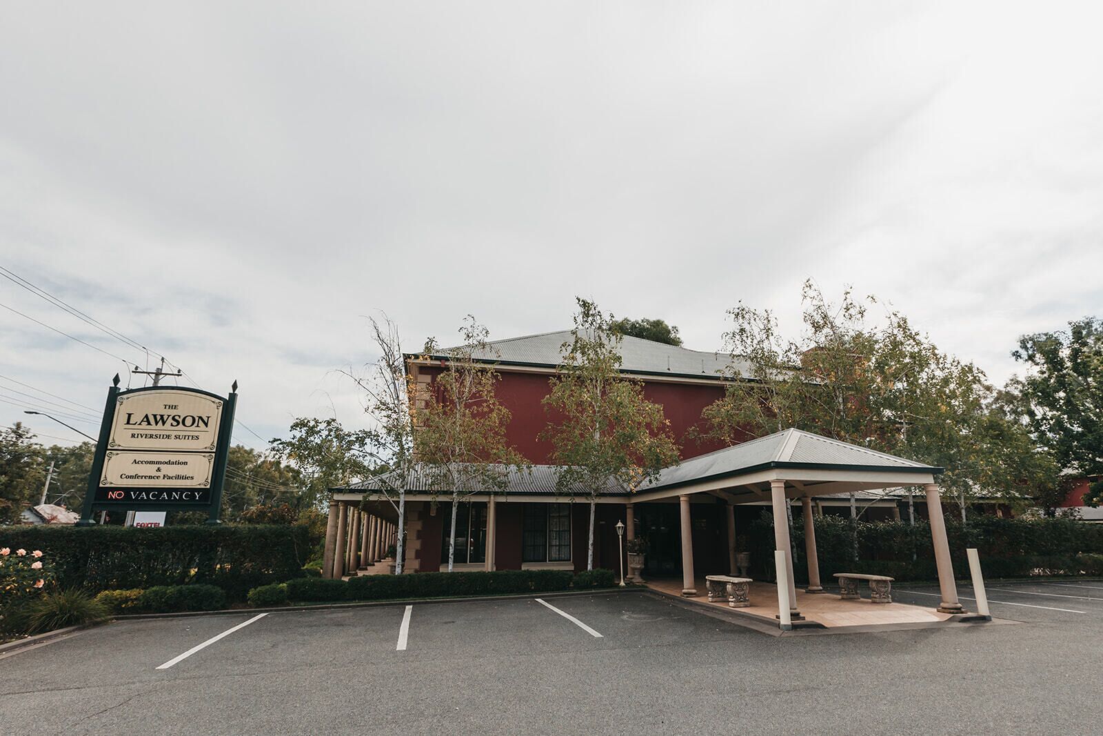 A building with a sign reading "The Lawson Riverside Suites" and a covered outdoor seating area.