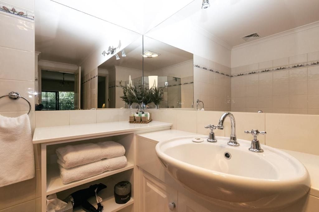A bathroom with a large mirror, a sink with two faucets, and a towel rack.