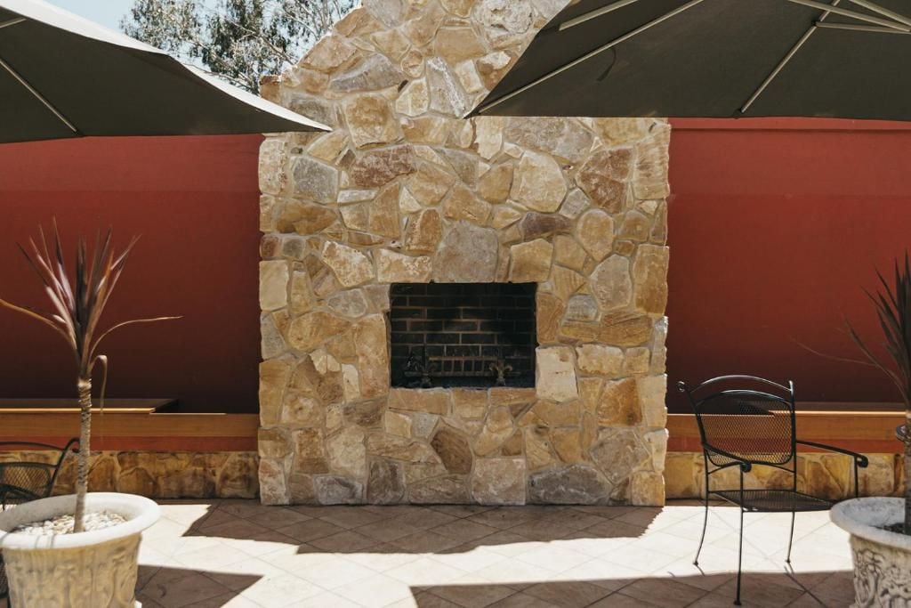 A stone fireplace with a fire, surrounded by outdoor seating and potted plants.