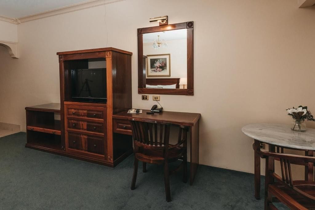 A room with a wooden desk, a chair, a small round table, and a large mirror on the wall.