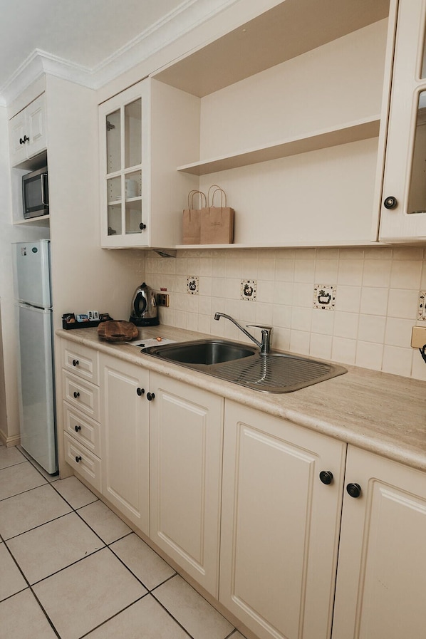 A kitchen with white cabinets, a stainless steel sink, a microwave, and a kettle.
