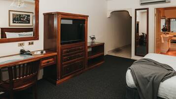 Una habitación de hotel con un escritorio de madera, un televisor, un espejo y una cama.