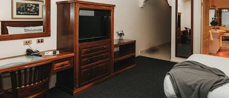 Une chambre d’hôtel avec un bureau en bois, une télévision, un miroir et un lit.