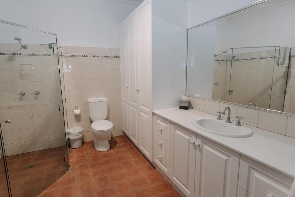 A bathroom with a glass-enclosed shower, a toilet, and a sink with a large mirror.