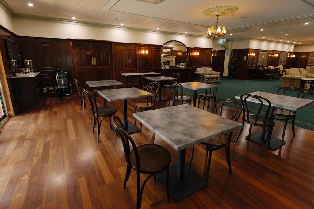 A hotel lobby with wooden flooring, multiple tables and chairs, a bar area, and a chandelier.