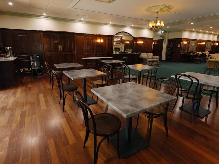Un vestíbulo de hotel con suelo de madera, varias mesas y sillas, una zona de bar y un candelabro.