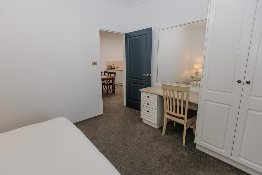 Quarto com cama, escrivaninha, cadeira, guarda-roupa e porta para um banheiro.