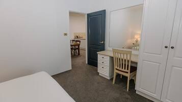Un dormitorio con una cama, un escritorio, una silla, un armario y una puerta que da a un baño.