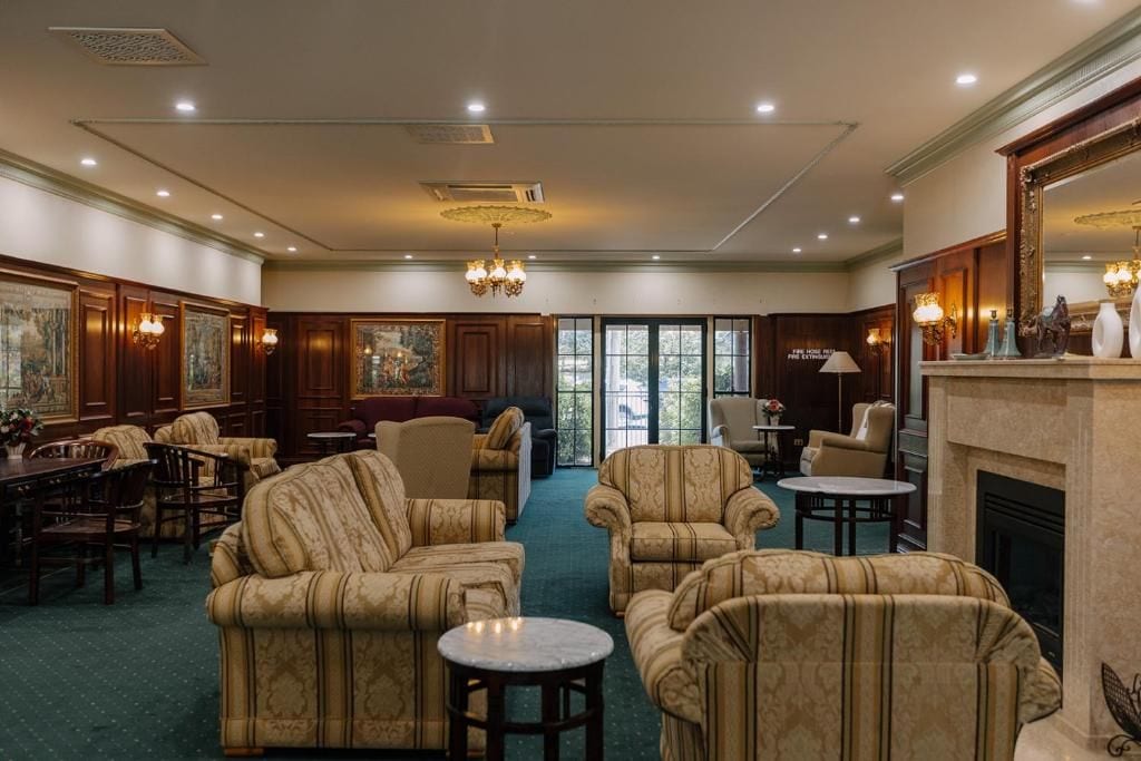 A spacious lounge area with multiple seating options, including sofas and armchairs, arranged around a central fireplace.
