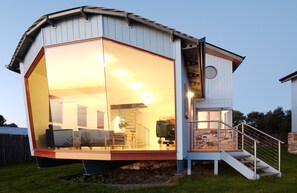 A modern house with a glass-enclosed living area, a staircase leading to a second floor, and a visible kitchen area. - Wheelhouse Apartments (Strahan)