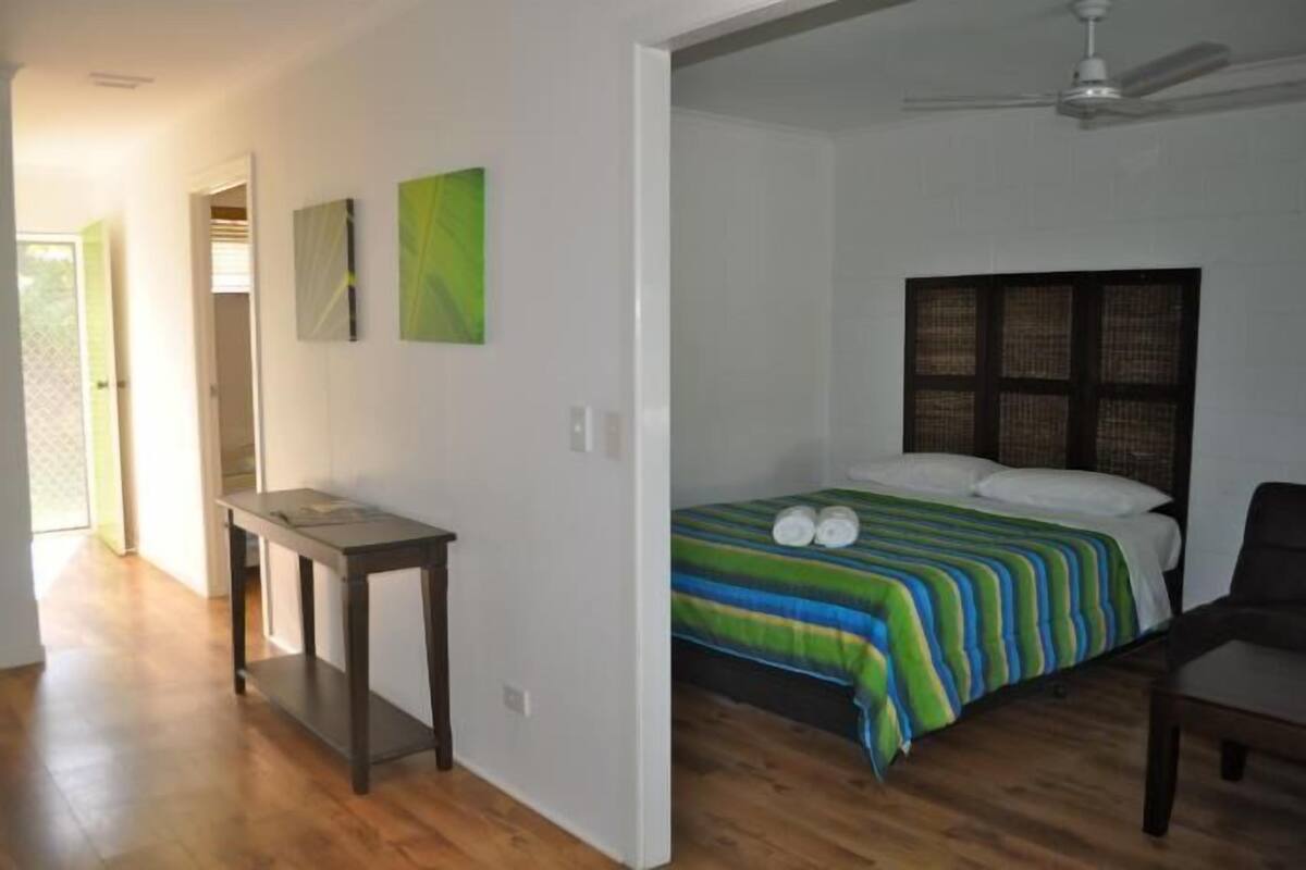 A bedroom with a bed, a table, and a chair. There is a door leading to another room.