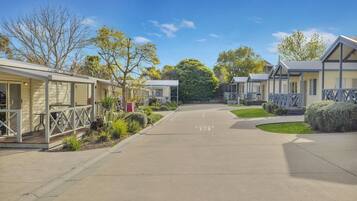 A row of single-story mobile homes with attached porches, a paved driveway, and a small parking area.