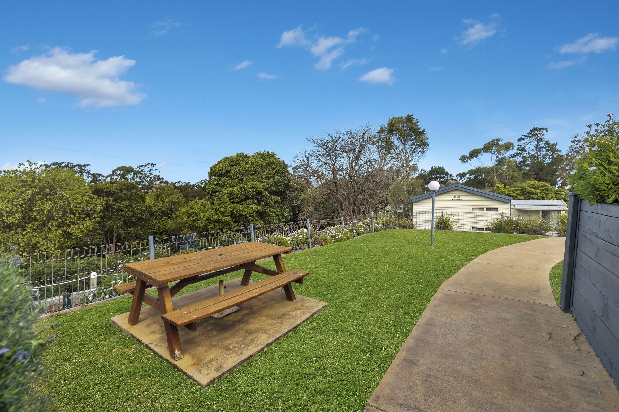 Una mesa de picnic en un área con césped, una cerca y un edificio al fondo.