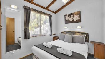 Une chambre à coucher avec un grand lit, une tête de lit ornée d’un motif floral, une fenêtre avec des rideaux, un miroir et un tableau accroché au mur.