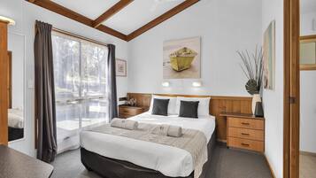 A bedroom with a large bed, wooden headboard, bedside tables, a nightstand, a window with curtains, and a painting on the wall.