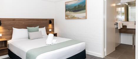 A hotel room with a bed, nightstands, a painting, and a bathroom visible through an open door.