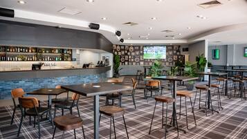 Un moderno bar con barra, asientos y una pantalla grande mostrando un evento deportivo.