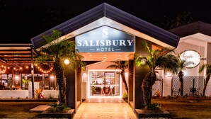 Het uiterlijk van het Salisbury Hotel, met een goed verlichte ingang, palmbomen en een zichtbaar bargedeelte.