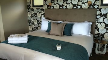 Cama bem arrumada com manta azul-turquesa, travesseiros brancos e cabeceira marrom.