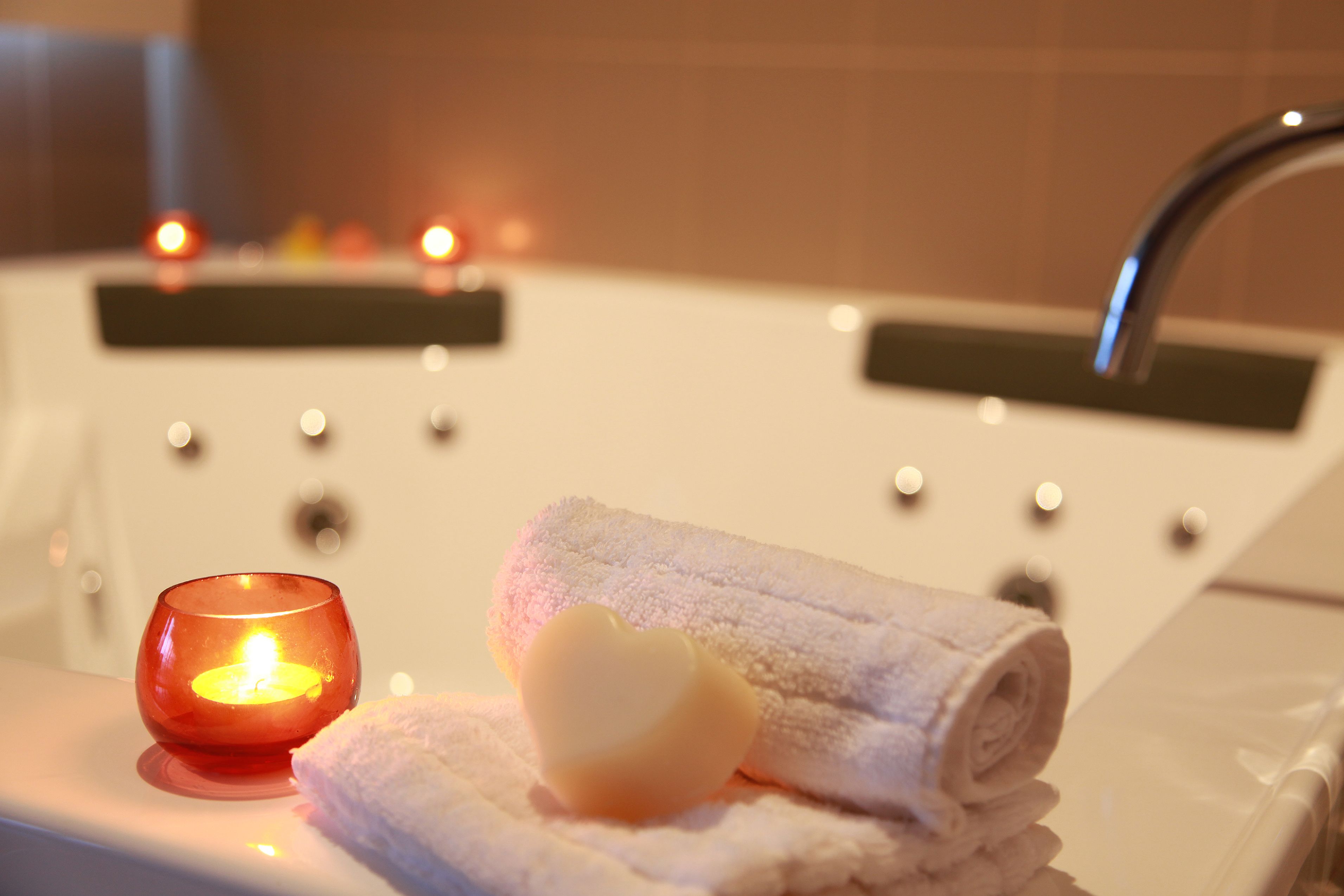 Un baño con bañera, una vela encendida y una toalla enrollada.