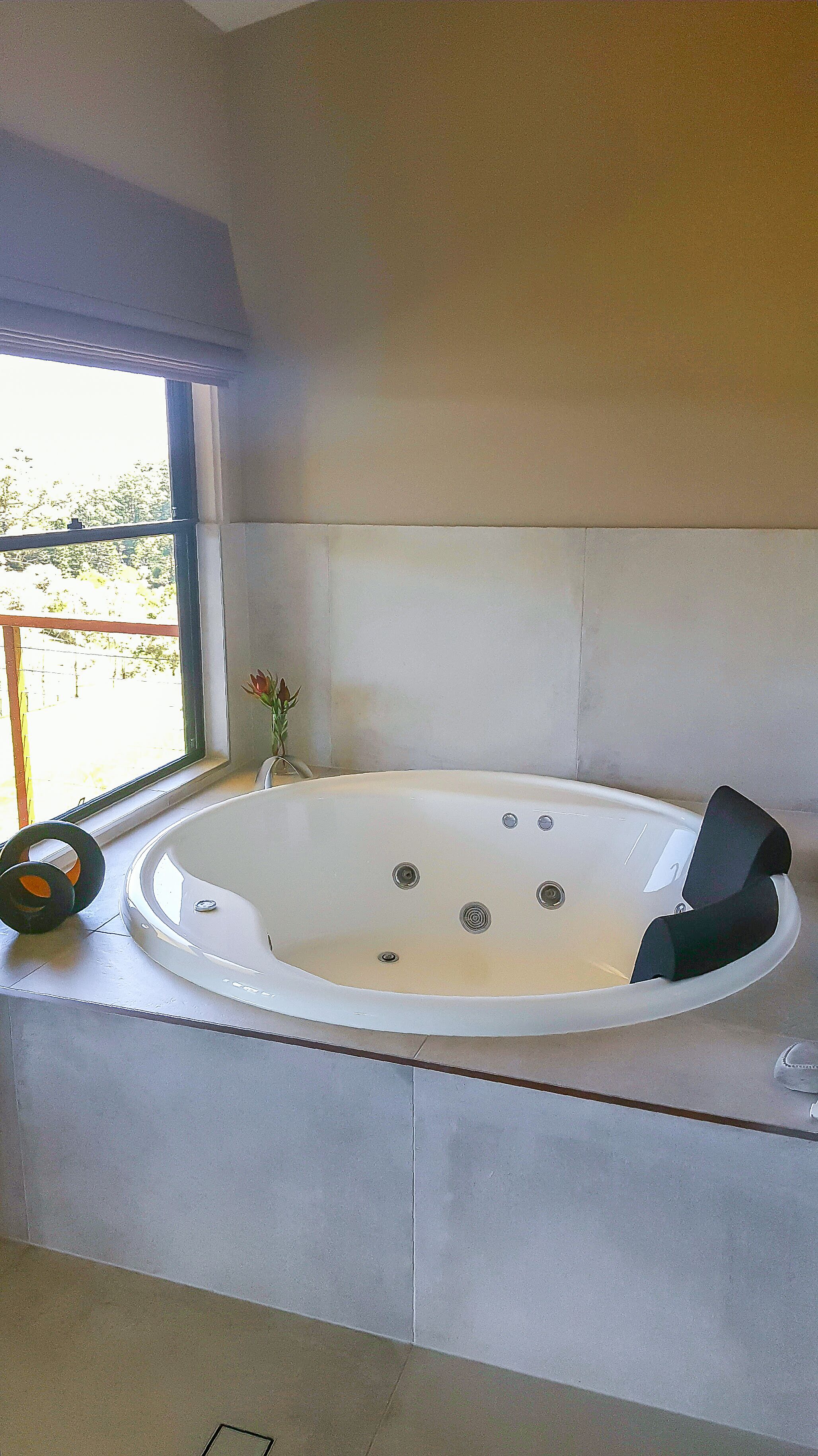 A modern bathroom with a freestanding bathtub, a window with a view of greenery, and a small vase with flowers on the windowsill.