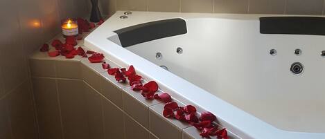 A corner bathroom with a bathtub, tiled walls, a window, and a vase with flowers.