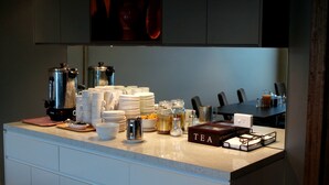 A kitchen counter with a coffee maker, stacks of white cups, and a tea box.