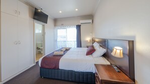 A hotel room with a bed, a nightstand, a TV, a window with curtains, and a wardrobe.