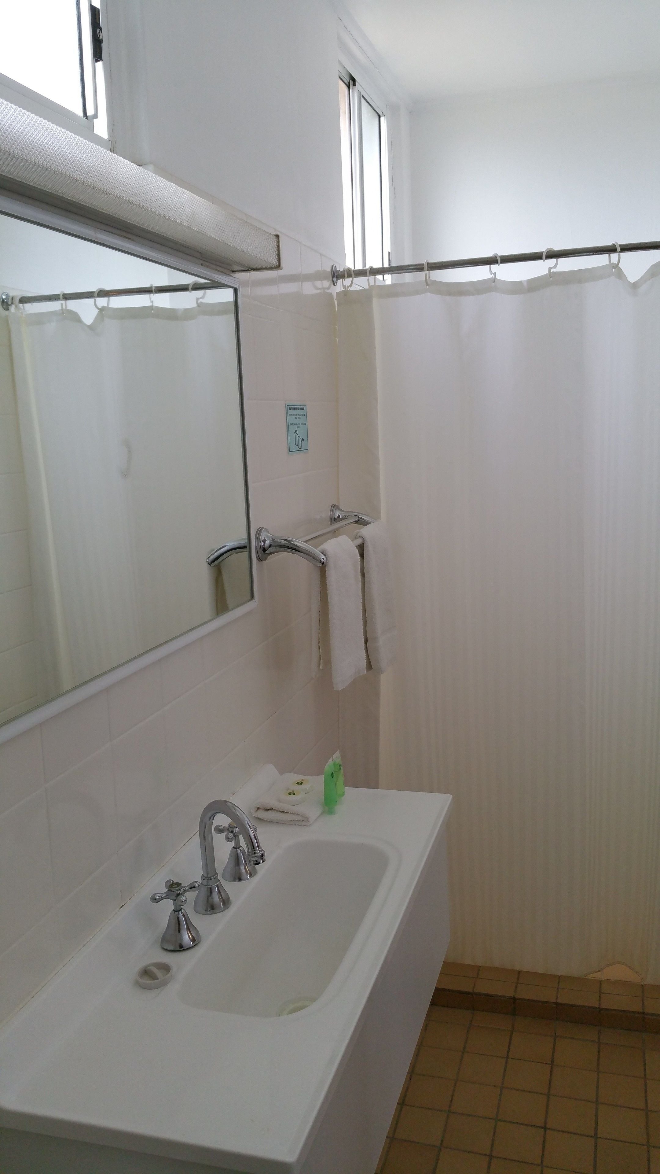 Une salle de bain avec un lavabo blanc, un miroir et un rideau de douche.