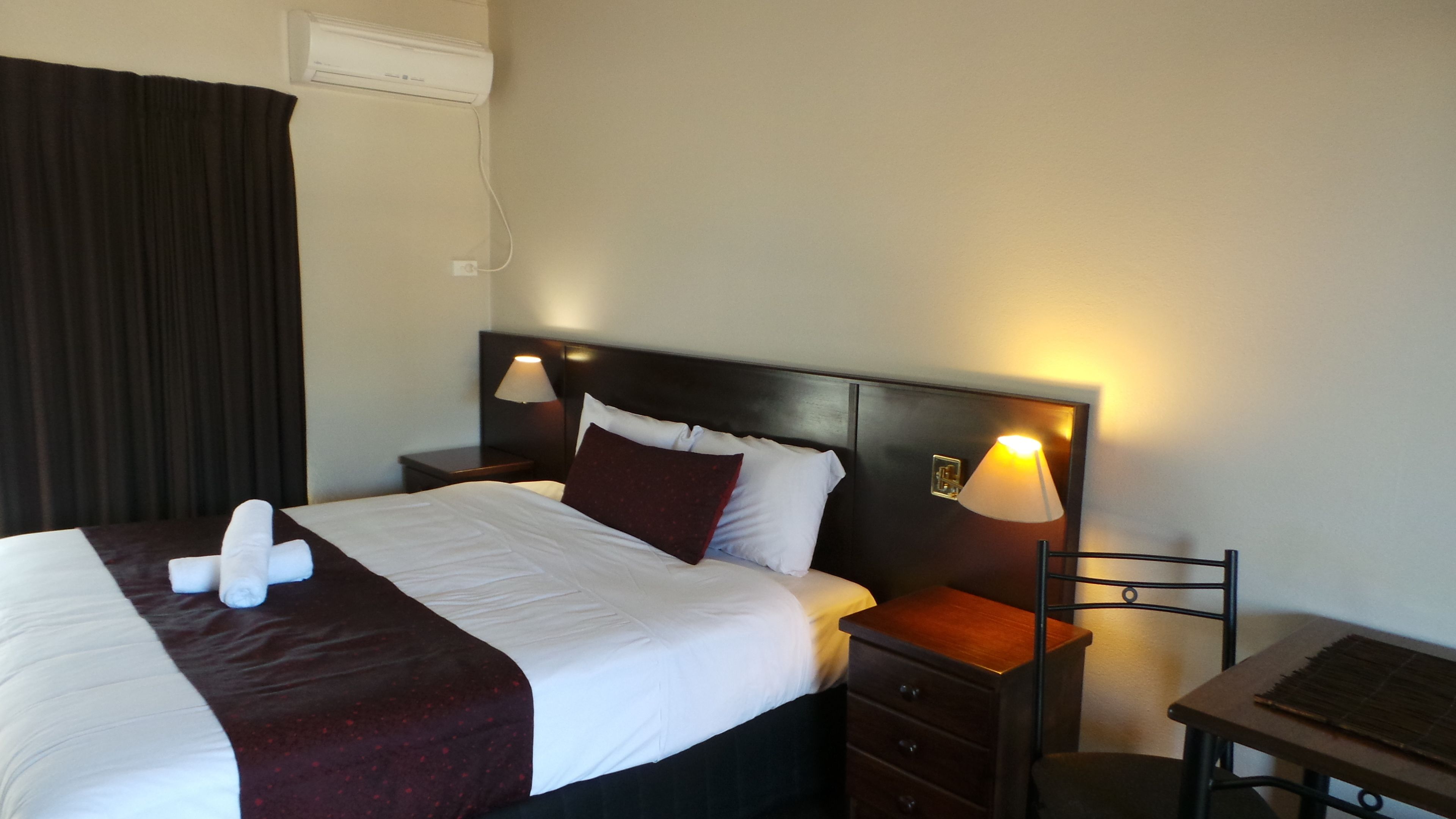Una habitación de hotel con una cama, dos mesitas de noche, una lámpara y una pequeña mesa con una silla.