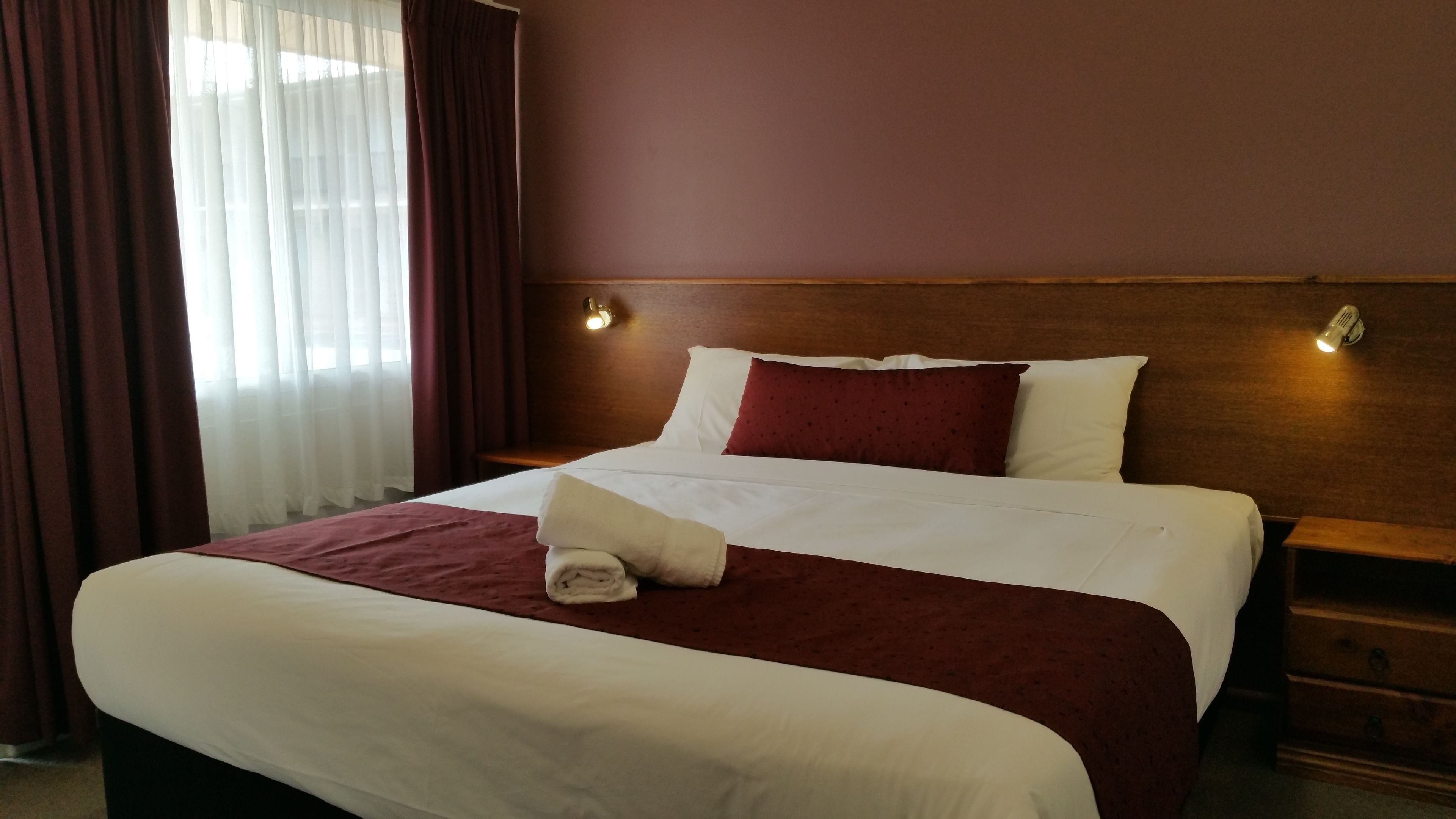 A hotel room with a large bed, a wooden headboard, two bedside tables, and a window with curtains.