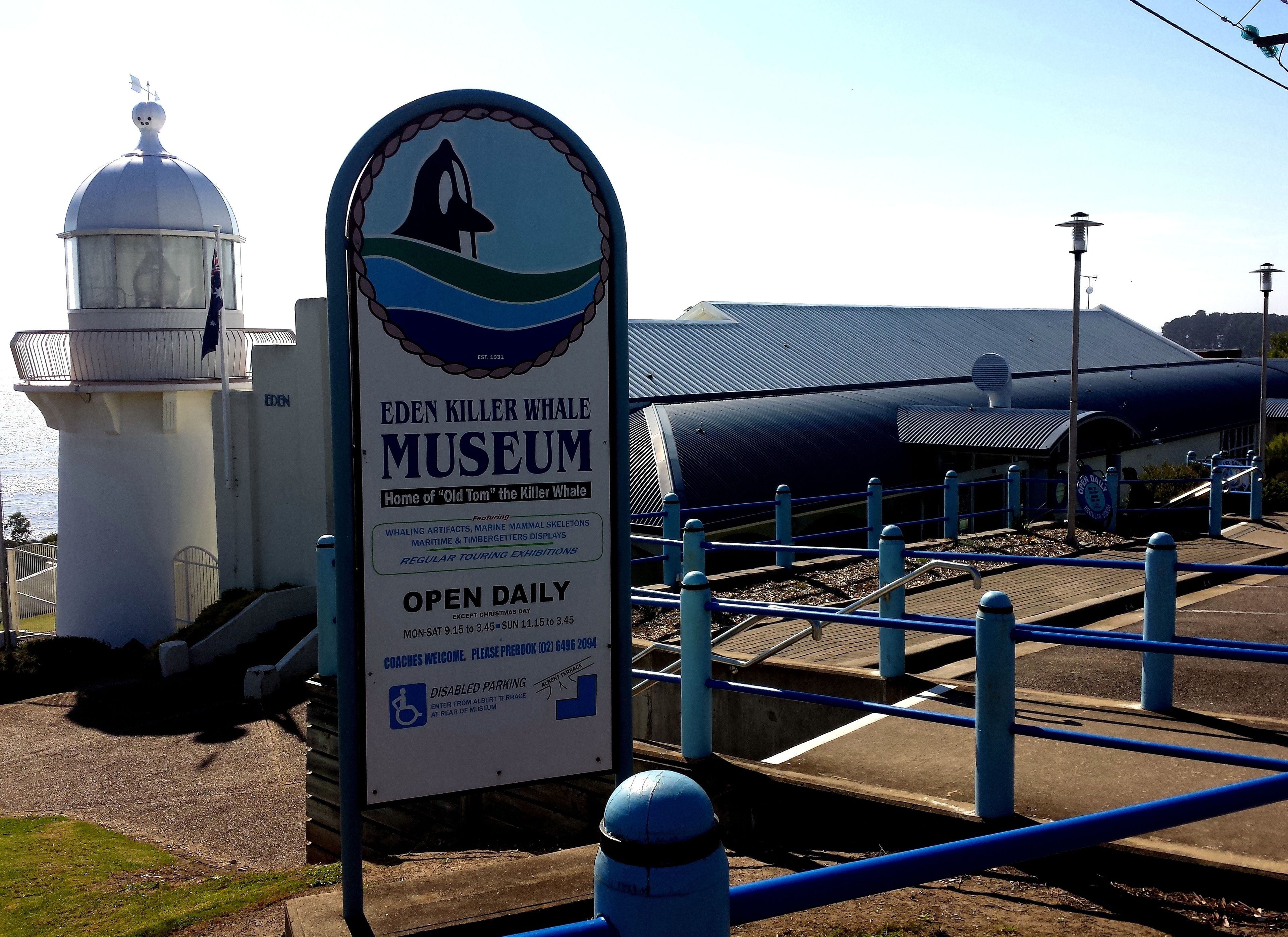 Une enseigne indiquant l'emplacement du musée Eden Killer Whale Museum, avec un phare en arrière-plan.