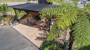 An outdoor seating area with tables and chairs, surrounded by lush greenery and a covered structure.