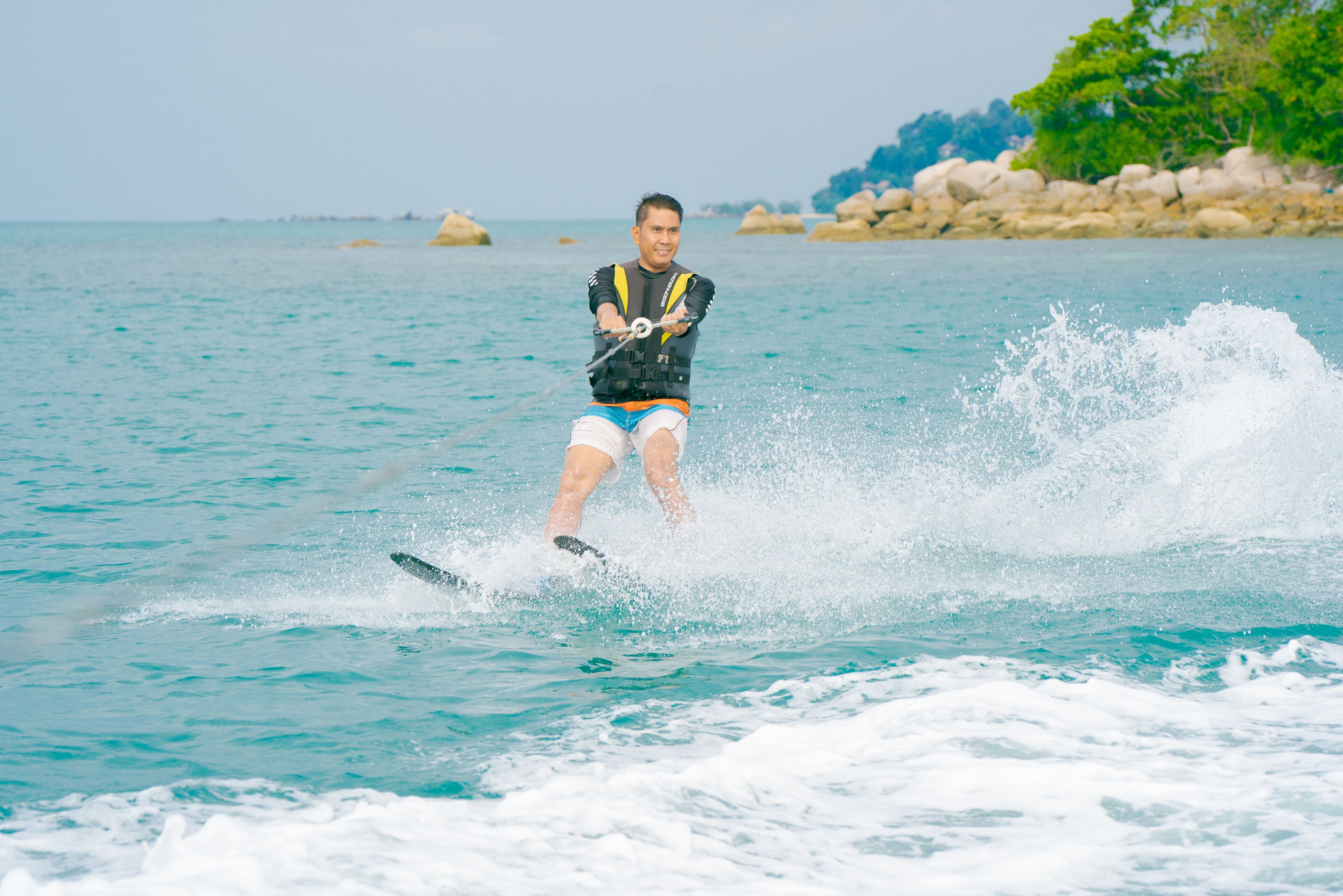 A person wakeboarding on a body of water with rocks and greenery in the background.