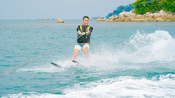 A person wakeboarding on a body of water with rocks and greenery in the background.