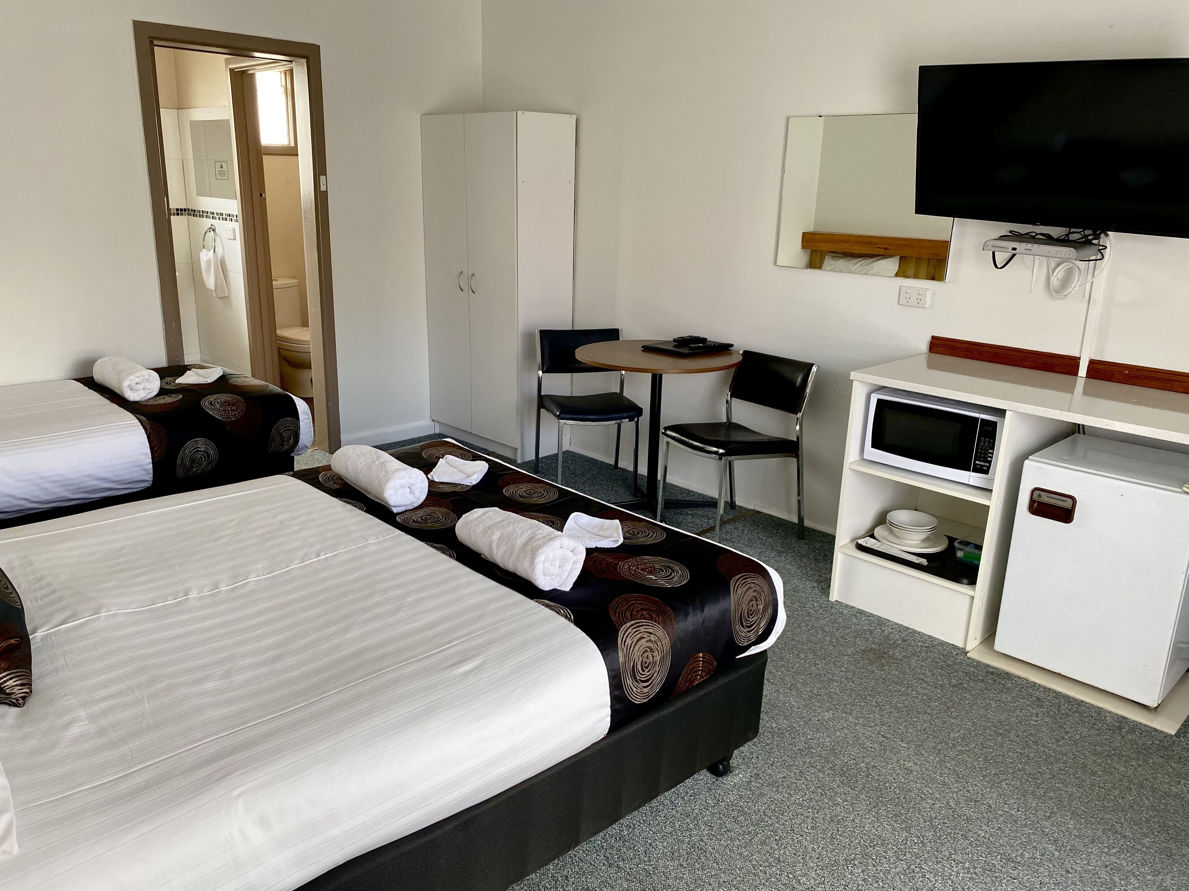 Een hotelkamer met twee bedden, een bureau, een stoel, een televisie, een magnetron en een minibar.
