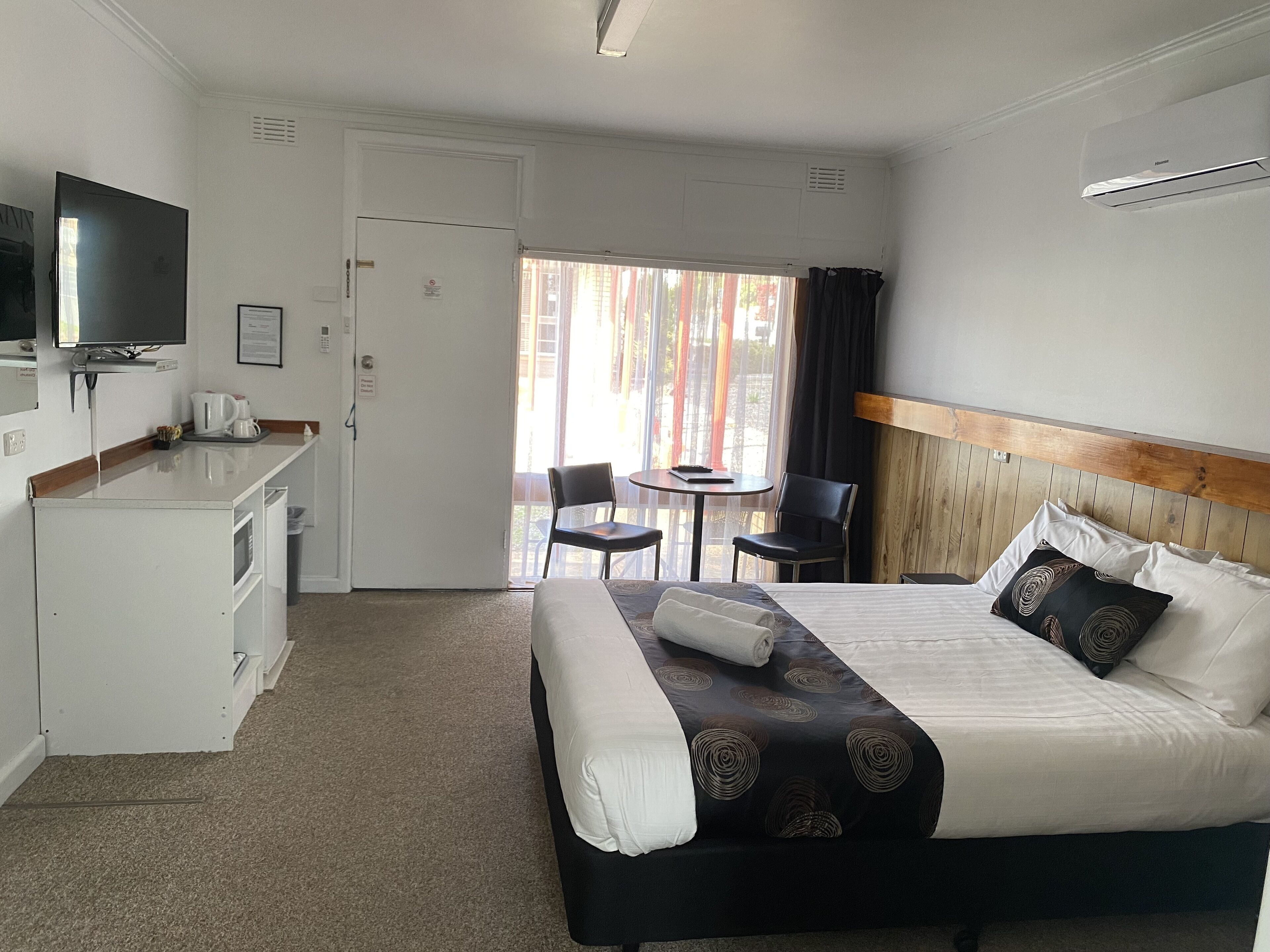 A hotel room with a bed, a desk with a television, a coffee maker, and a window with curtains.