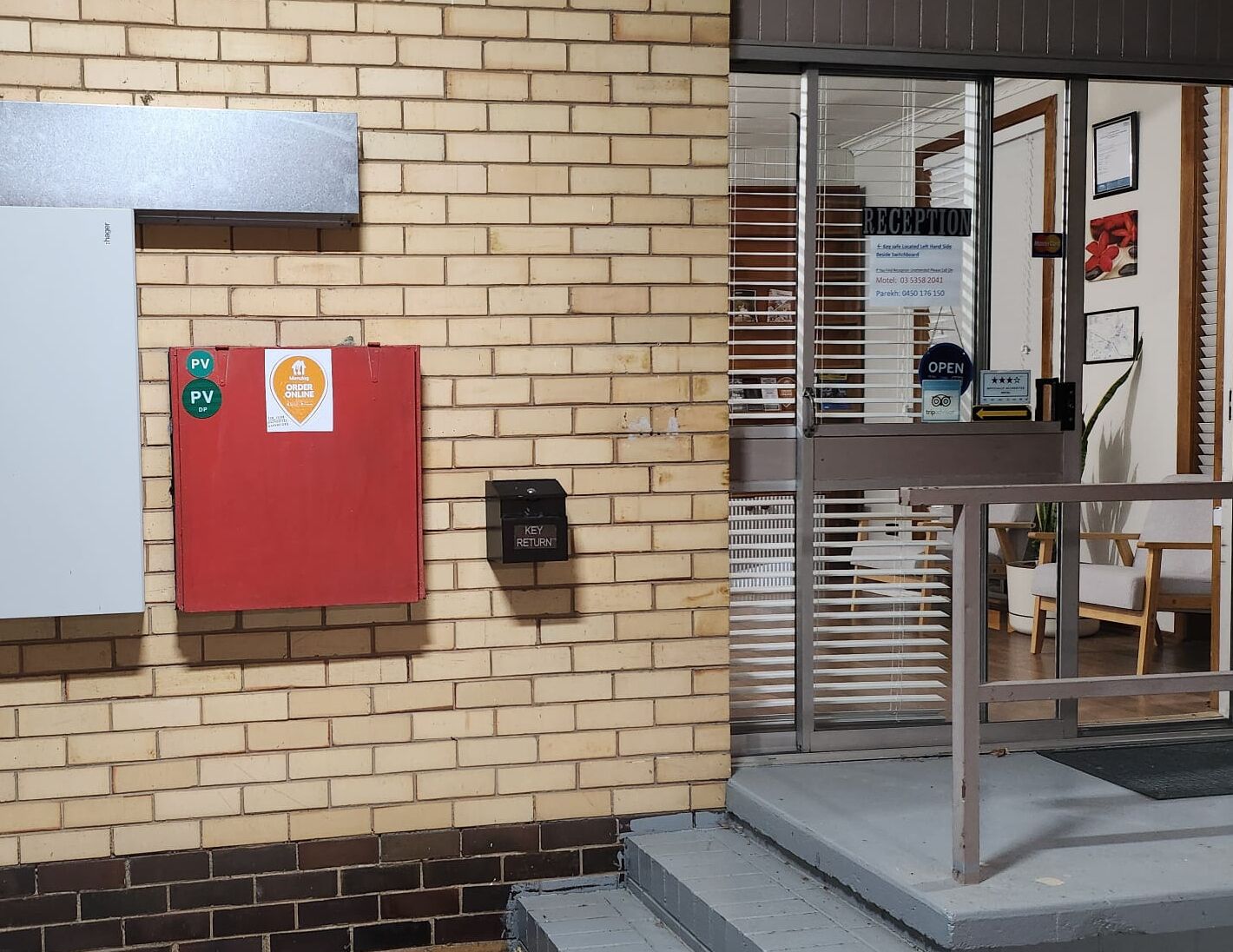 A hotel entrance with a reception desk, a key return box, and a PV (parking) sign.