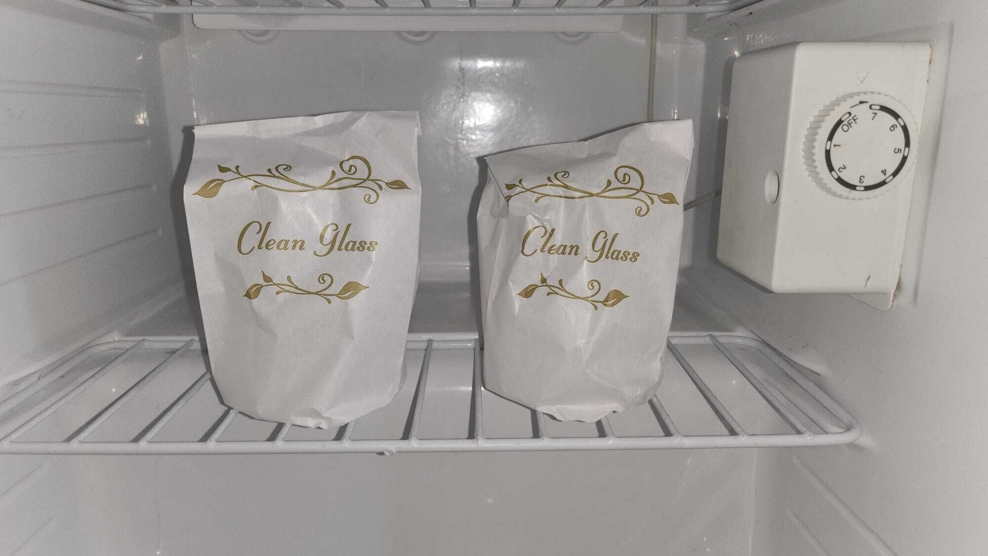 Un refrigerador limpio y vacío con dos bolsas etiquetadas como 'Clean Glass' en los estantes de la puerta.