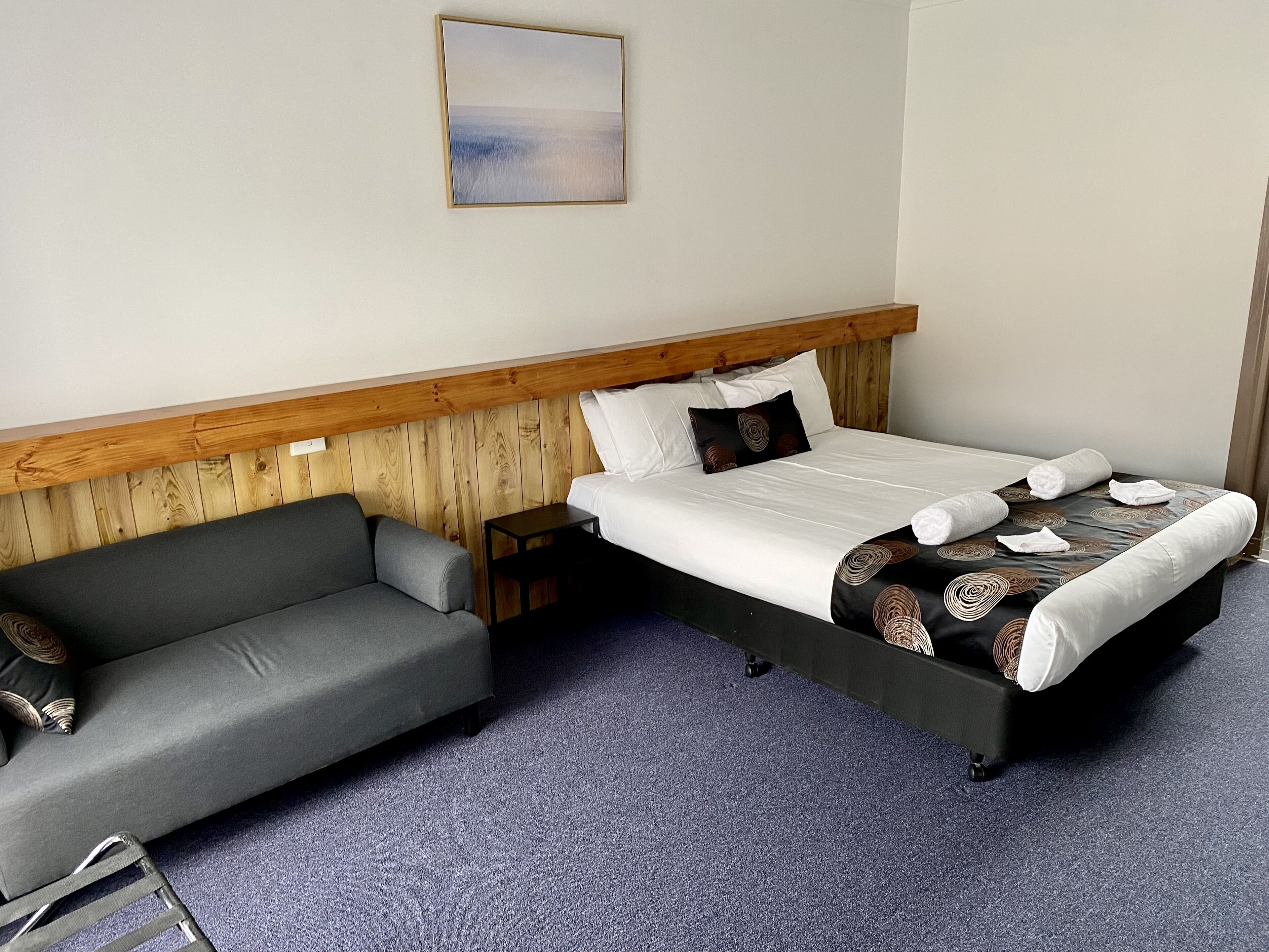 A hotel room with a bed, a grey sofa, a small table, and a wooden headboard.