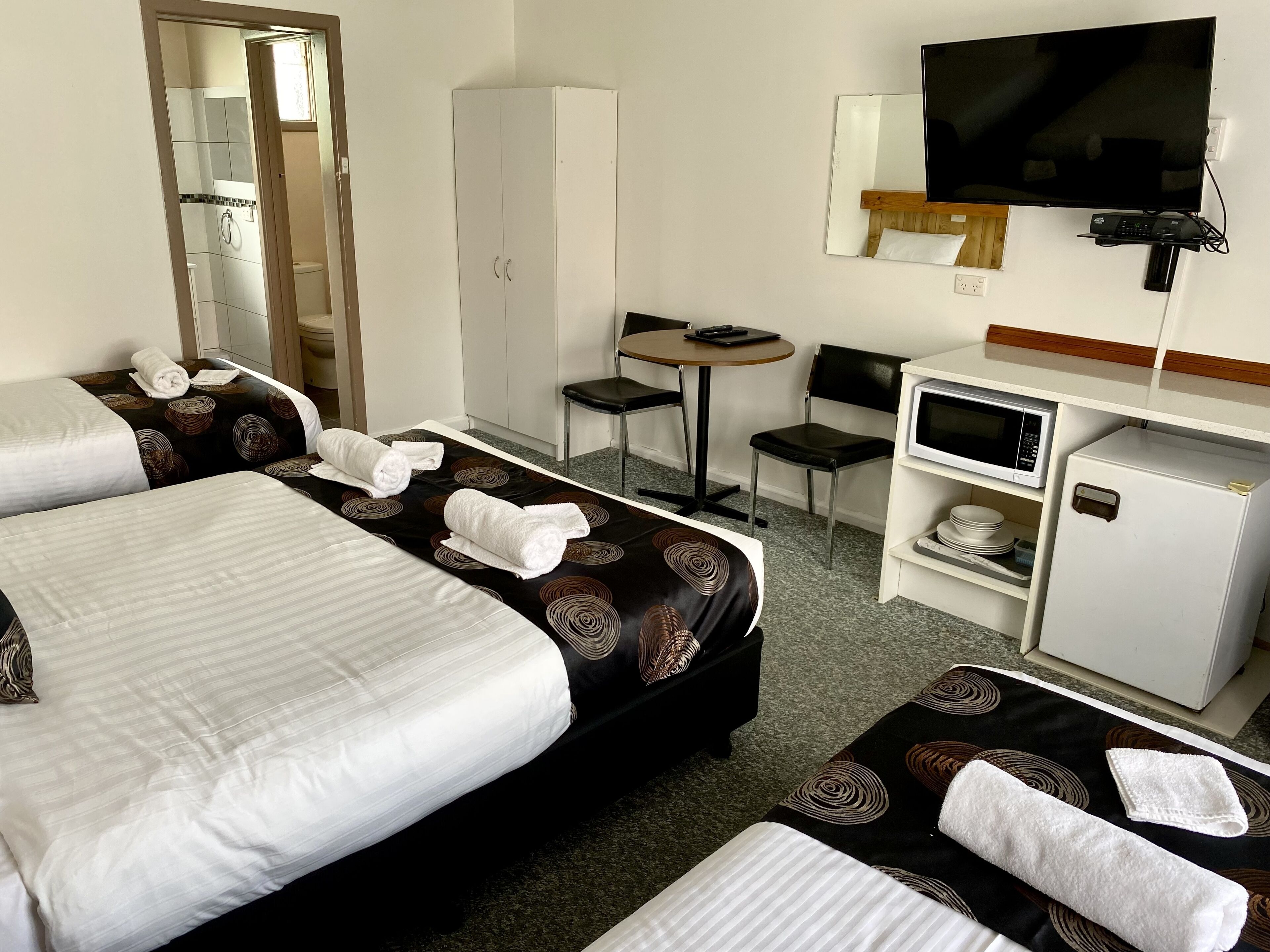 Et hotelværelse med to senge, et skrivebord, en stol, et fjernsyn, en mikrobølgeovn og et køleskab.
