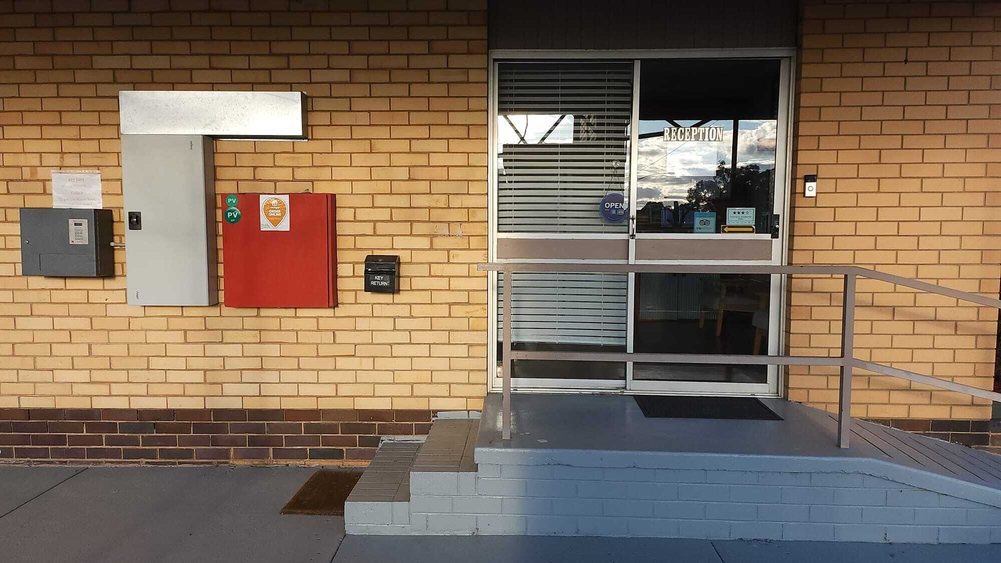 Entrada de un edificio con mostrador de recepción, buzón para devolución de llaves y caja de alarma contra incendios.