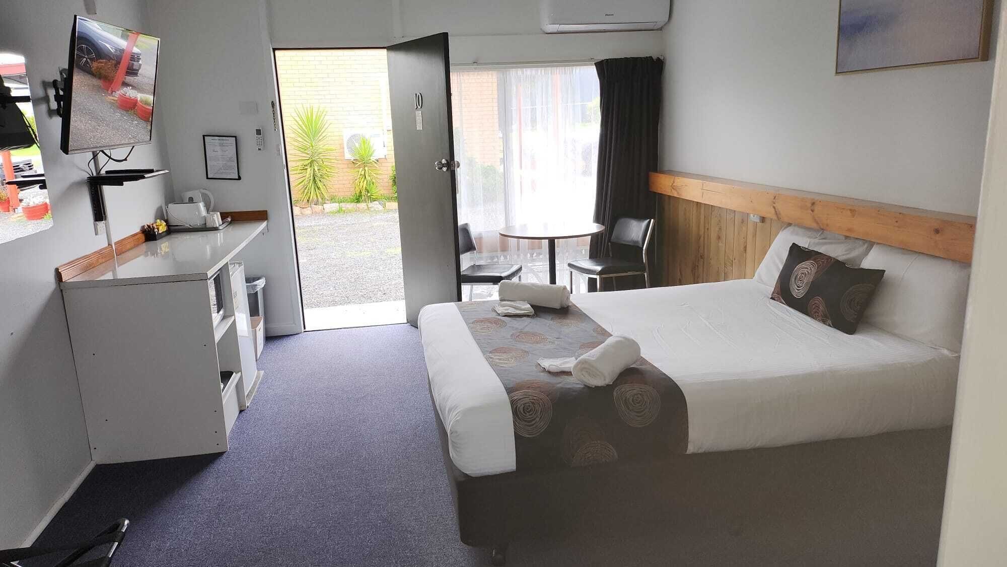 A hotel room with a bed, a desk, a chair, a small table, and a TV.