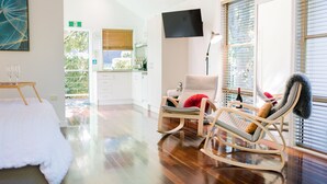 Una habitación moderna con una cama, un sillón mecedora, un televisor montado en la pared y vistas al exterior.