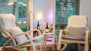 Una habitación con dos mecedoras, una mesita con una botella de vino y una copa, y vistas al exterior a través de una ventana con persianas.