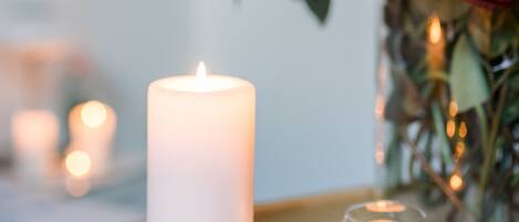 A white candle in a glass holder, surrounded by smaller candles and a bouquet of flowers.