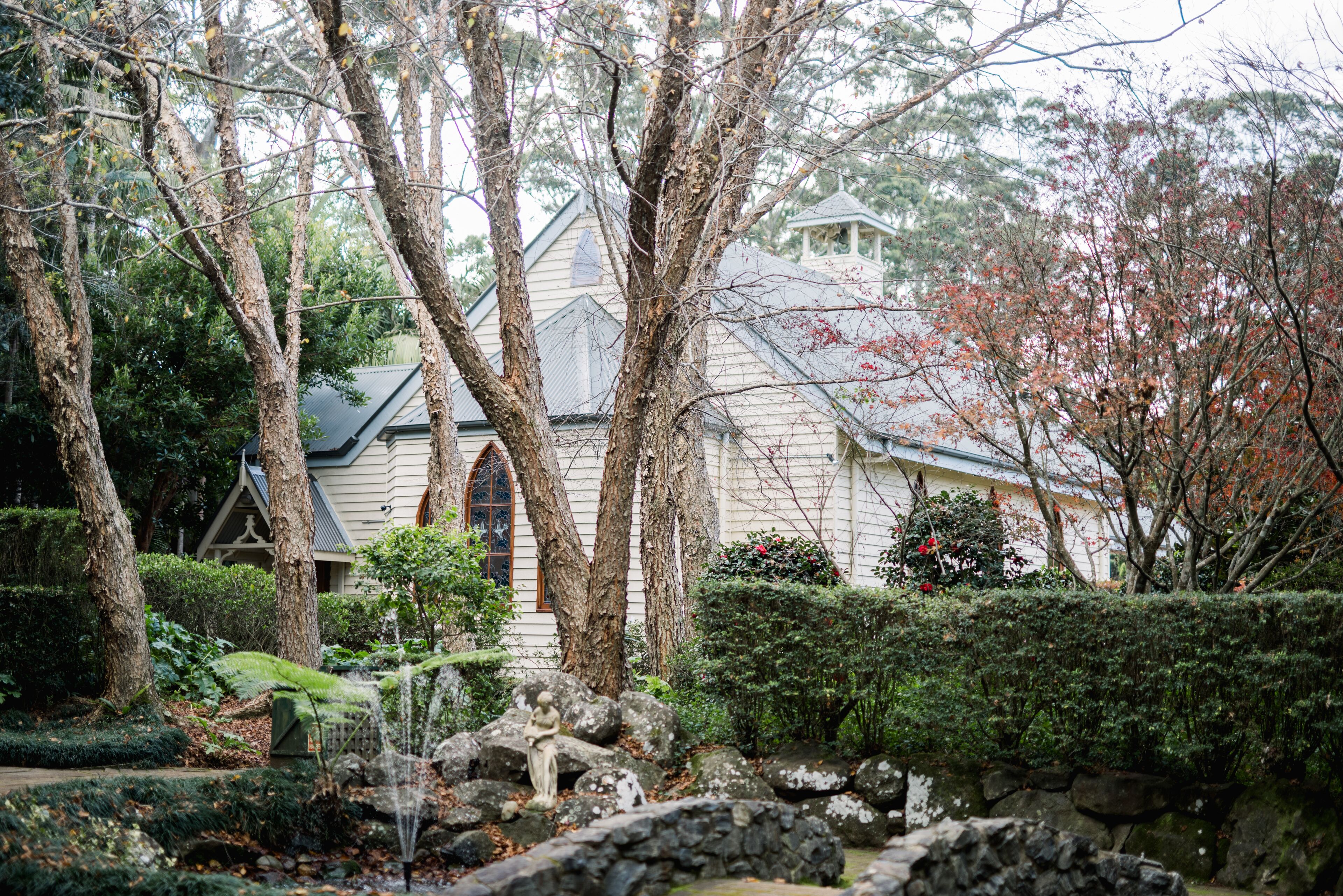 A serene garden with a stone fountain, lush greenery, and a building with a distinctive architectural style.