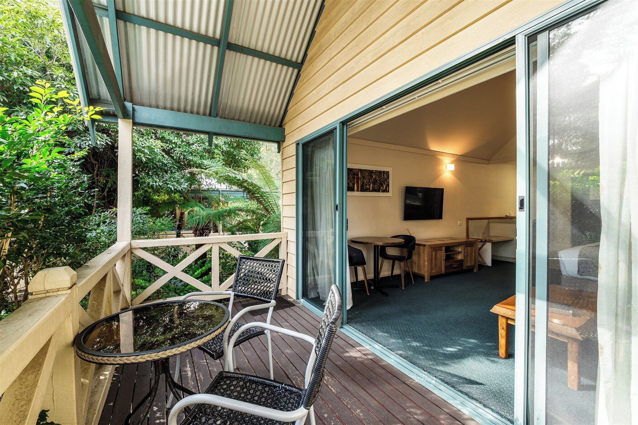 A covered outdoor area with a table and chairs, a sliding glass door leading to an interior space with a bed and a TV.