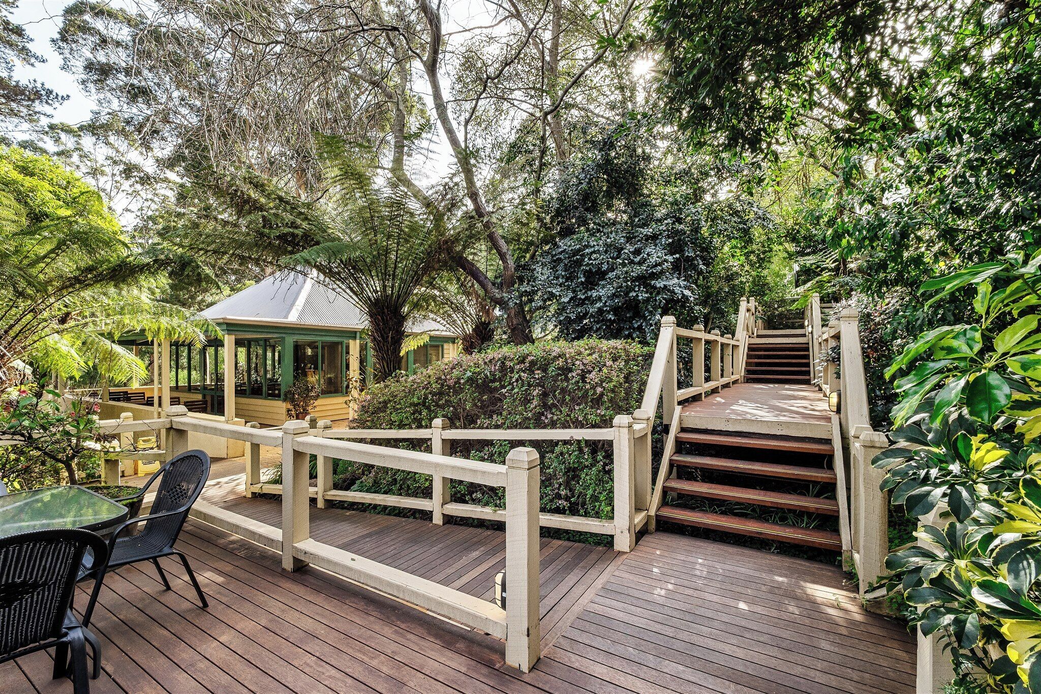 A wooden deck with a railing, a gazebo, and a staircase surrounded by lush greenery.