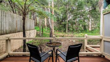 Eine Holzterrasse mit zwei Stühlen und einem Tisch, mit Blick auf ein bewaldetes Gebiet mit Holzzaun und einem Gebäude im Hintergrund.